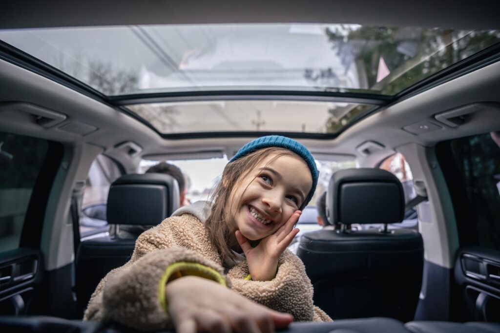 Funny little girl posing in the back seat of a car, playing in the car.