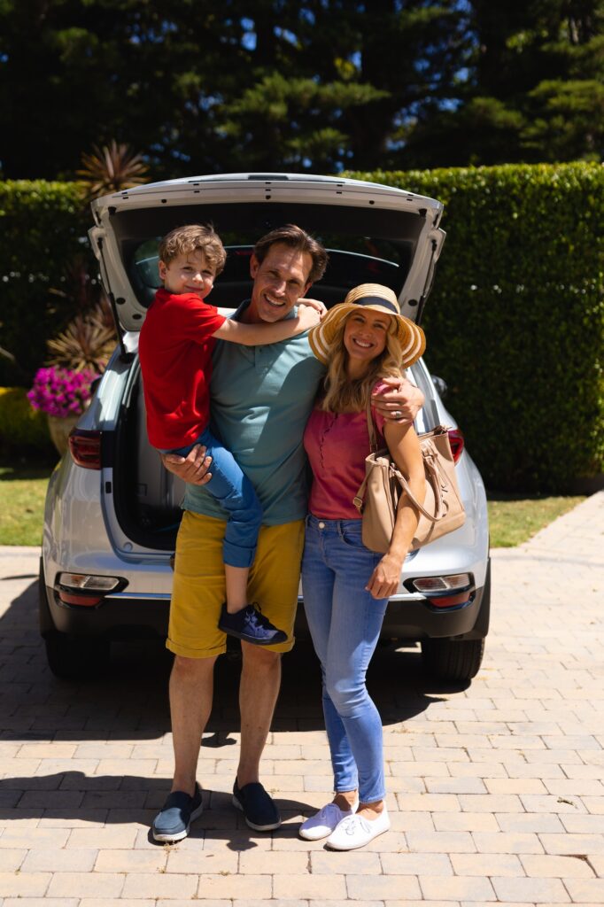 Portrait of happy caucasian family standing near their car outdoors